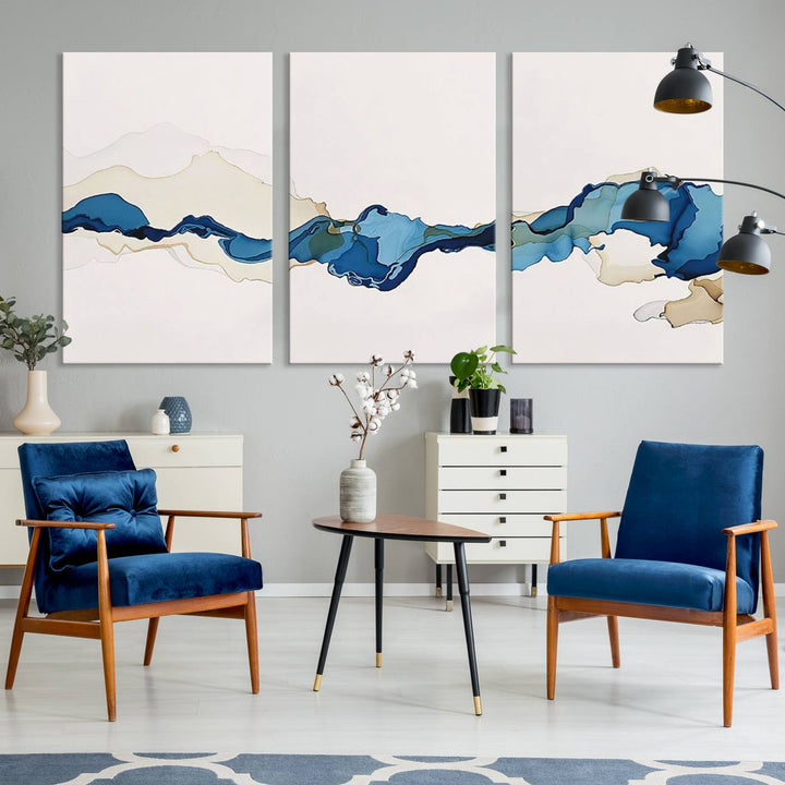 The modern living room showcases a set of three canvas prints with abstract blue art on museum-quality materials.