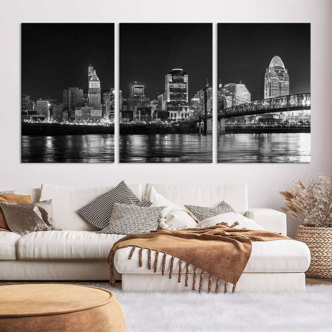 The Cincinnati City Lights Skyline Black and White Wall Art Cityscape Canvas Print elegantly adorns a modern living room. This museum-quality canvas triptych of a city skyline is enhanced by hand-assembled frames for added finesse, and you can enjoy free shipping on this stunning home addition.