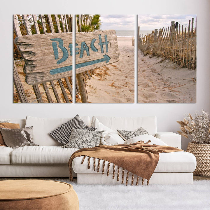 The Beach Is Calling You Wall Art Canvas Print features a sandy beach path with a wooden beach sign and arrow pointing to the ocean, beautifully displayed on museum-quality canvases.