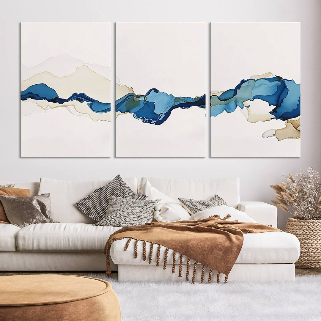 The modern living room showcases a set of three canvas prints with abstract blue art on museum-quality materials.