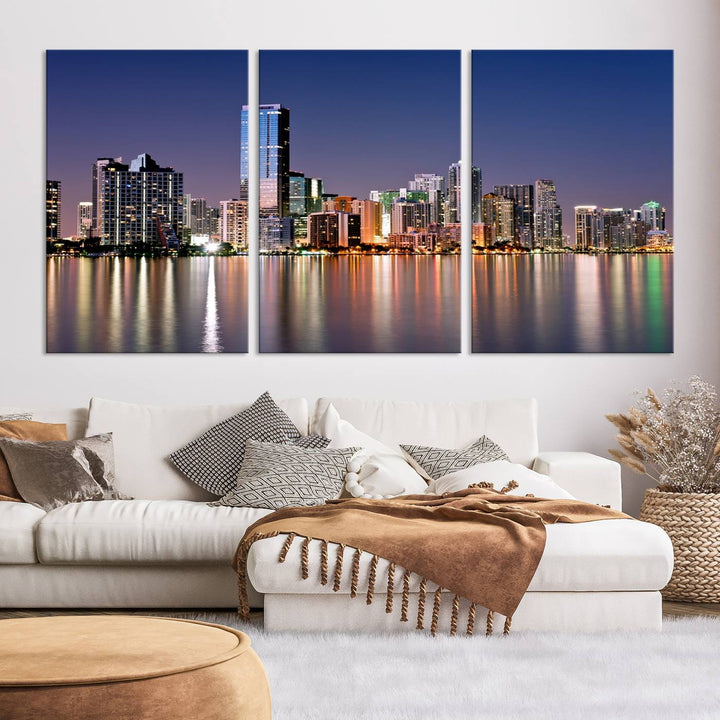 The Miami Skyline Canvas Wall Art Print showcases a vibrant night cityscape and beautifully captures the dazzling colorful lights reflecting on the water. This ready-to-hang triptych adorns the wall, creating a stunning visual centerpiece.