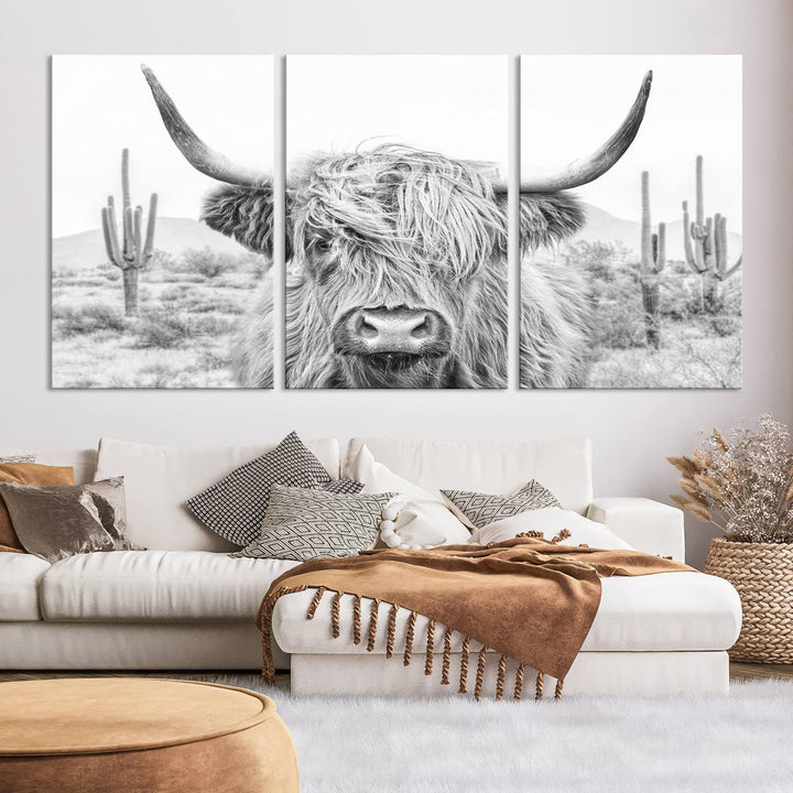 The "Rustic Charm | Cow Longhorn Black White Bighorn Wall Art Canvas Print" is a stunning triptych that showcases a highland cow with long horns set against a desert landscape with cacti in the background. This farmhouse wall art elevates any room into a rustic haven with its gallery-quality canvas.