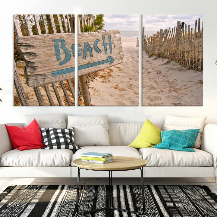 The Beach Is Calling You Wall Art Canvas Print features a sandy beach path with a wooden beach sign and arrow pointing to the ocean, beautifully displayed on museum-quality canvases.