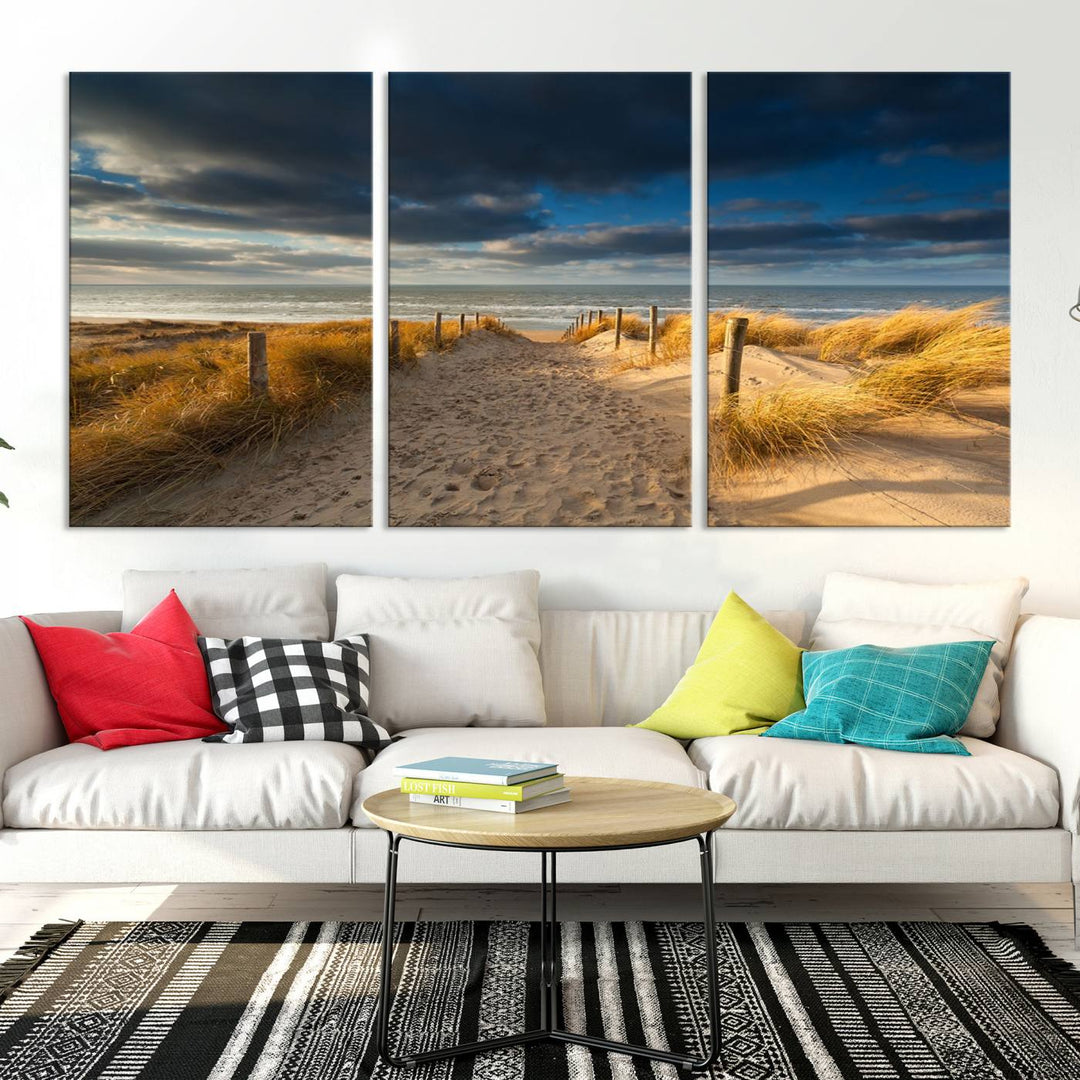 The Ocean Beach Dark Clouds Wall Art Canvas Print is a breathtaking triptych depicting a sandy beach path with tall grasses under an intense cloudy sky. It is crafted on museum-quality canvas with UV protection.