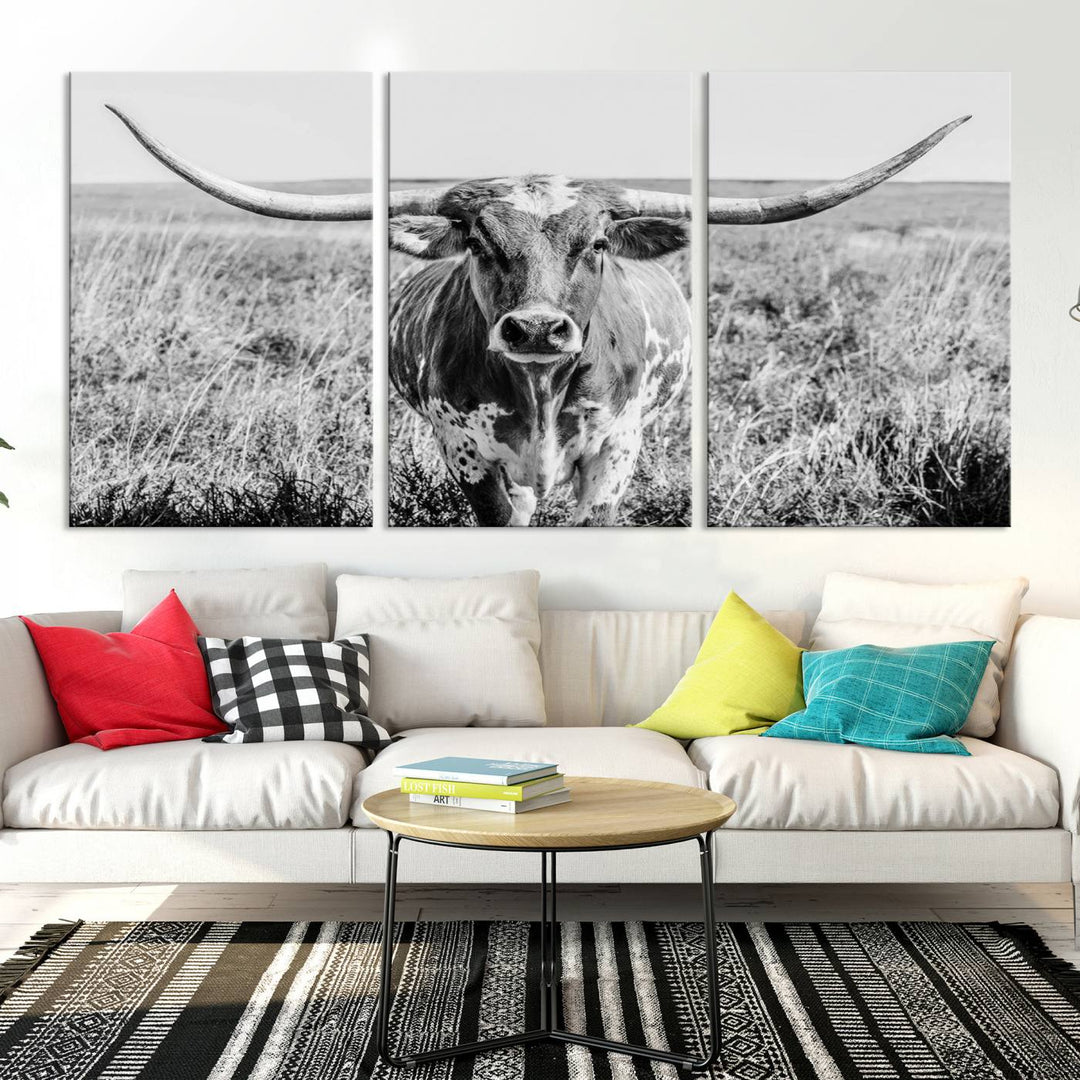 The Texas Cow Longhorn Wall Art Canvas Print is a black and white triptych depicting a cow in a field. It is crafted with museum-quality canvas and features a UV-protective coating.