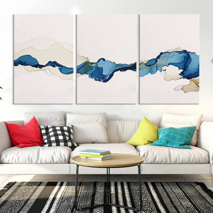 The modern living room showcases a set of three canvas prints with abstract blue art on museum-quality materials.