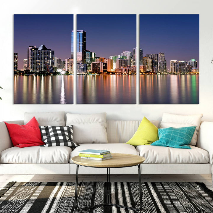 The Miami Skyline Canvas Wall Art Print showcases a vibrant night cityscape and beautifully captures the dazzling colorful lights reflecting on the water. This ready-to-hang triptych adorns the wall, creating a stunning visual centerpiece.