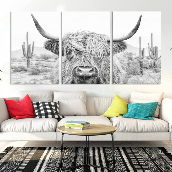 The "Rustic Charm | Cow Longhorn Black White Bighorn Wall Art Canvas Print" is a stunning triptych that showcases a highland cow with long horns set against a desert landscape with cacti in the background. This farmhouse wall art elevates any room into a rustic haven with its gallery-quality canvas.