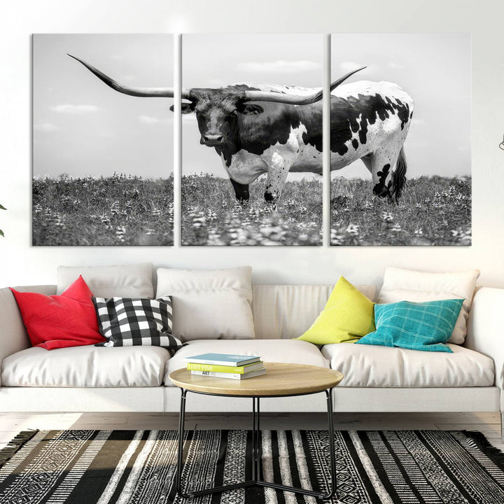 The Texas Black White Highland Longhorn Cow Wall Art Canvas Print, a gallery-quality triptych, elegantly adorns the wall, showcasing a striking black-and-white depiction of a longhorn cow in a field.