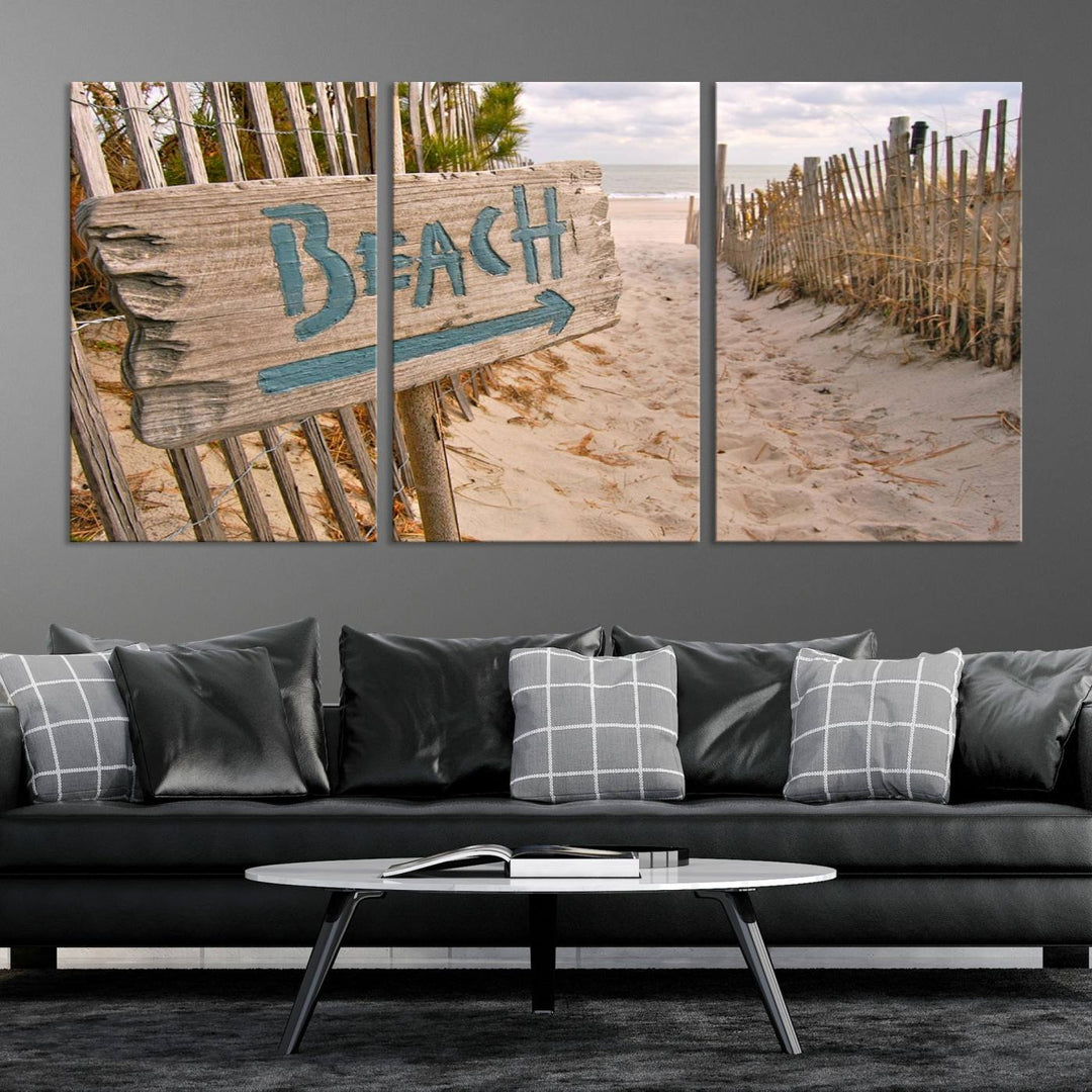 The Beach Is Calling You Wall Art Canvas Print features a sandy beach path with a wooden beach sign and arrow pointing to the ocean, beautifully displayed on museum-quality canvases.