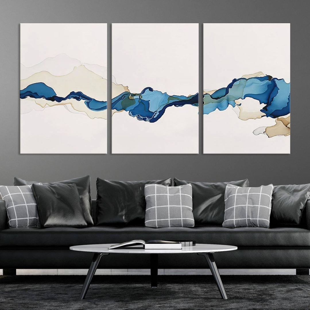 The modern living room showcases a set of three canvas prints with abstract blue art on museum-quality materials.