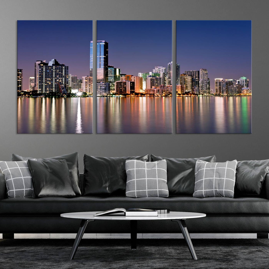 The Miami Skyline Canvas Wall Art Print showcases a vibrant night cityscape and beautifully captures the dazzling colorful lights reflecting on the water. This ready-to-hang triptych adorns the wall, creating a stunning visual centerpiece.