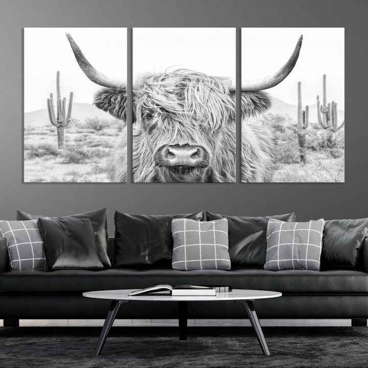 The "Rustic Charm | Cow Longhorn Black White Bighorn Wall Art Canvas Print" is a stunning triptych that showcases a highland cow with long horns set against a desert landscape with cacti in the background. This farmhouse wall art elevates any room into a rustic haven with its gallery-quality canvas.