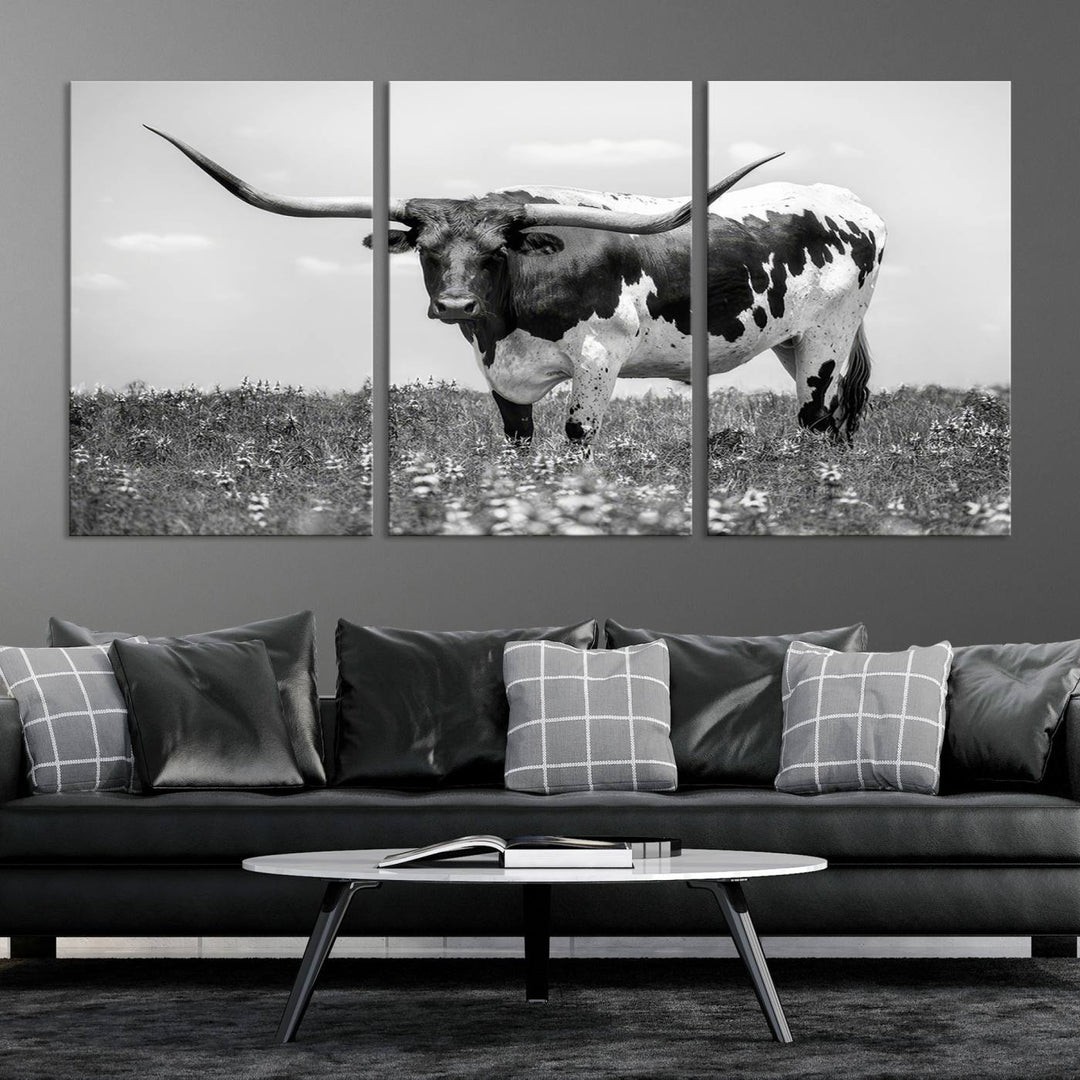 The Texas Black White Highland Longhorn Cow Wall Art Canvas Print, a gallery-quality triptych, elegantly adorns the wall, showcasing a striking black-and-white depiction of a longhorn cow in a field.