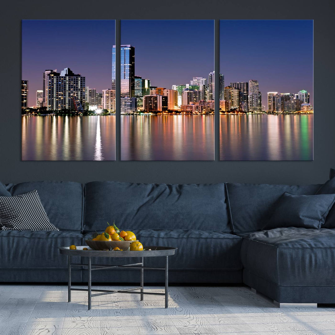 The Miami Skyline Canvas Wall Art Print showcases a vibrant night cityscape and beautifully captures the dazzling colorful lights reflecting on the water. This ready-to-hang triptych adorns the wall, creating a stunning visual centerpiece.