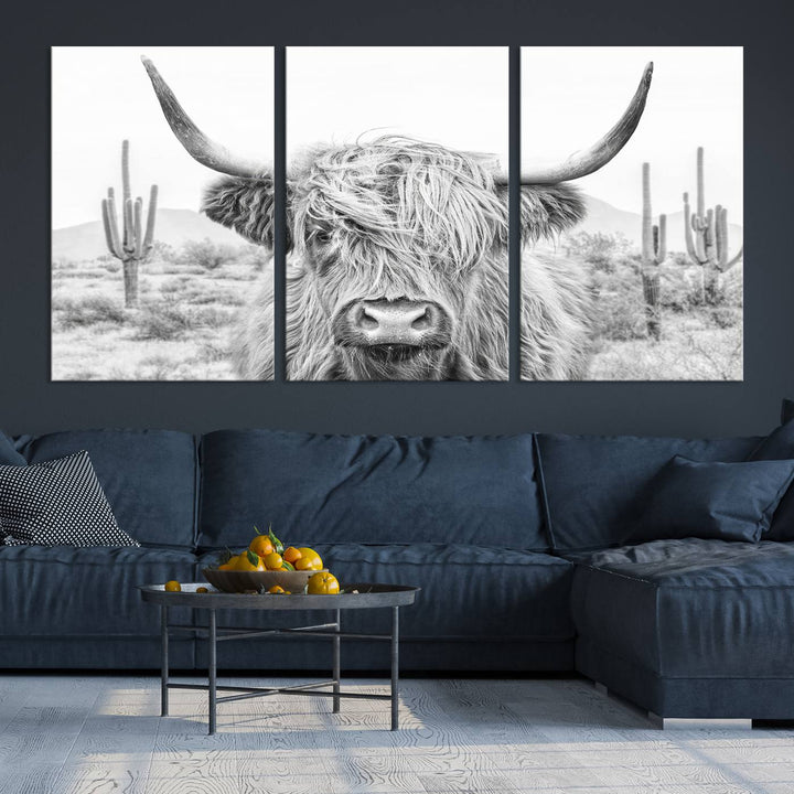 The "Rustic Charm | Cow Longhorn Black White Bighorn Wall Art Canvas Print" is a stunning triptych that showcases a highland cow with long horns set against a desert landscape with cacti in the background. This farmhouse wall art elevates any room into a rustic haven with its gallery-quality canvas.