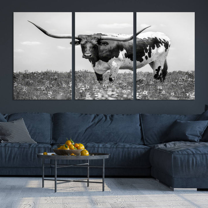 The Texas Black White Highland Longhorn Cow Wall Art Canvas Print, a gallery-quality triptych, elegantly adorns the wall, showcasing a striking black-and-white depiction of a longhorn cow in a field.