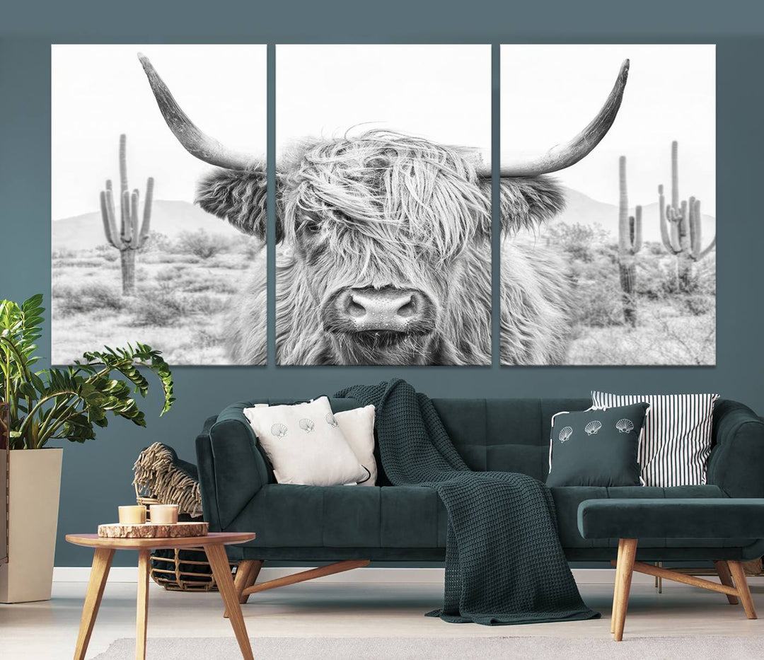 The "Rustic Charm | Cow Longhorn Black White Bighorn Wall Art Canvas Print" is a stunning triptych that showcases a highland cow with long horns set against a desert landscape with cacti in the background. This farmhouse wall art elevates any room into a rustic haven with its gallery-quality canvas.