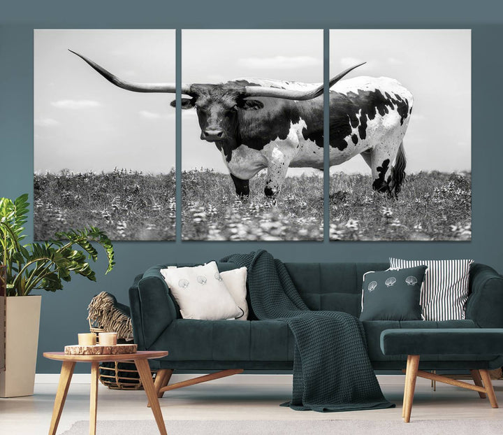 The Texas Black White Highland Longhorn Cow Wall Art Canvas Print, a gallery-quality triptych, elegantly adorns the wall, showcasing a striking black-and-white depiction of a longhorn cow in a field.