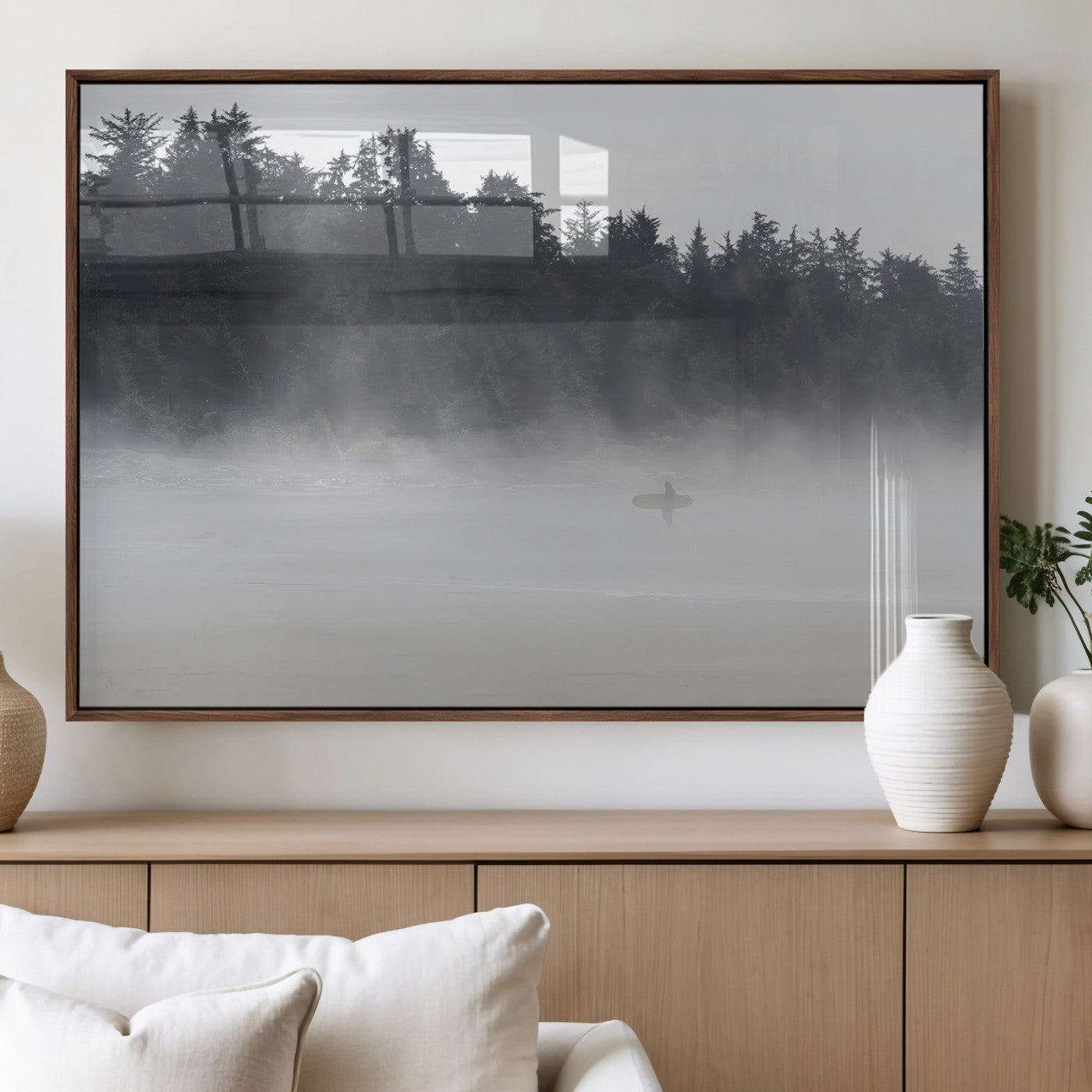 A lone surfer carrying a board through a misty shoreline, surrounded by dense trees and fog, creating a peaceful and mysterious coastal scene.
