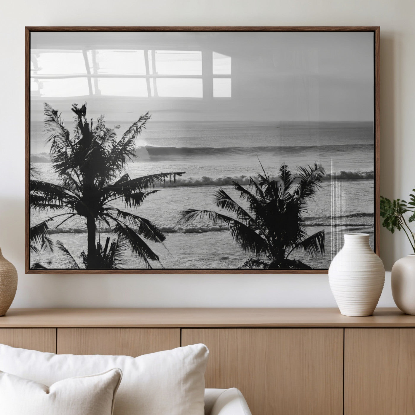 Black and white view of ocean waves crashing on a tropical coastline, framed by silhouetted palm trees under a vast, open sky.