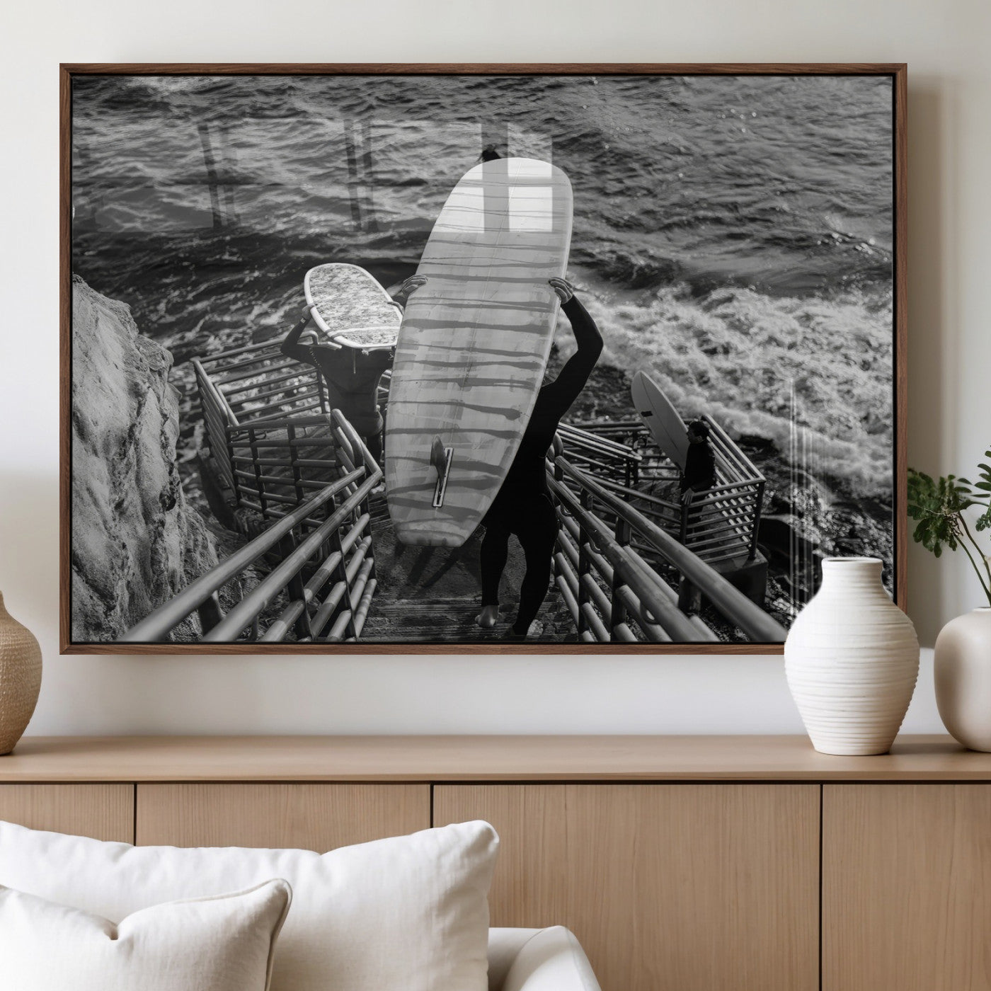 Black and white photo of surfers carrying boards down a rugged cliffside stairway, capturing a bold and adventurous coastal scene.