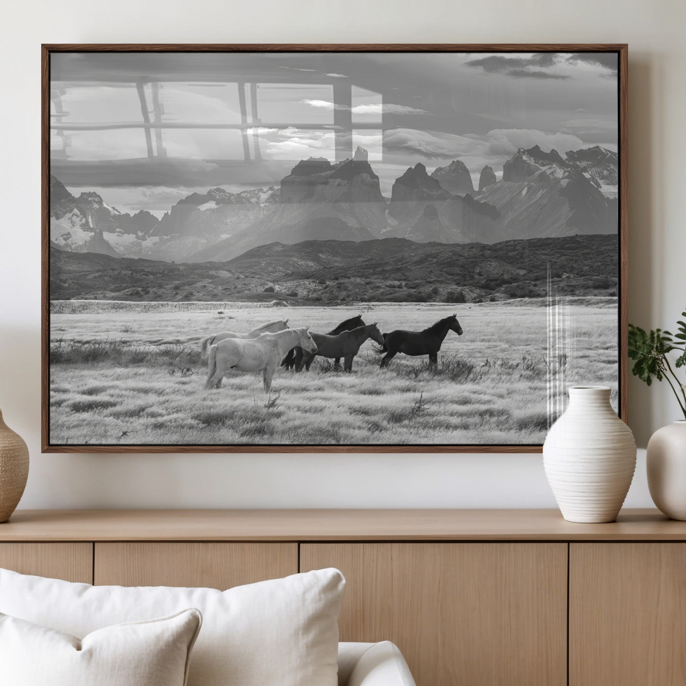 A black and white landscape of wild horses grazing in a vast grassland with towering mountains in the background, creating a moody and rustic western aesthetic.