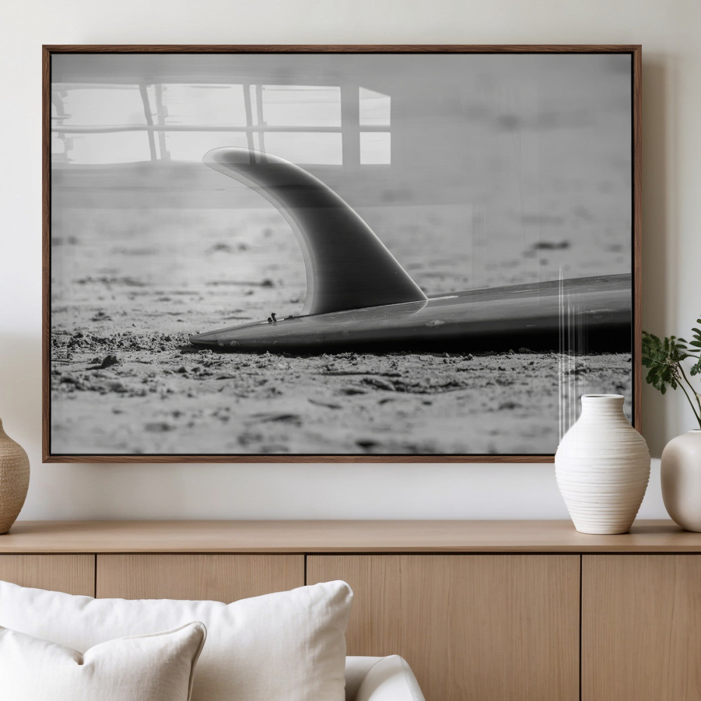 A black and white close-up of a surfboard fin resting on the sandy shore, highlighting minimalist beach aesthetics and classic surf culture.