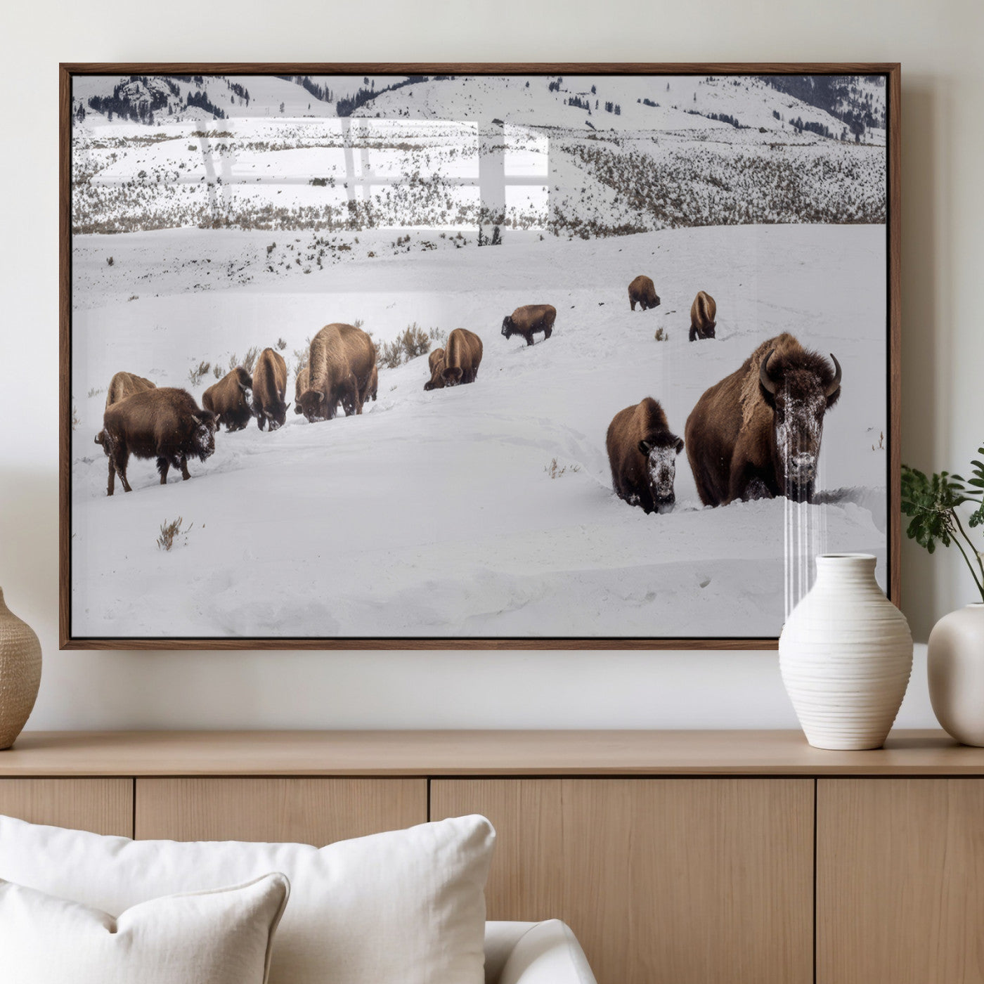 A herd of bison walking through deep snow in a mountain valley, perfect for rustic, cabin or western-themed wall decor.