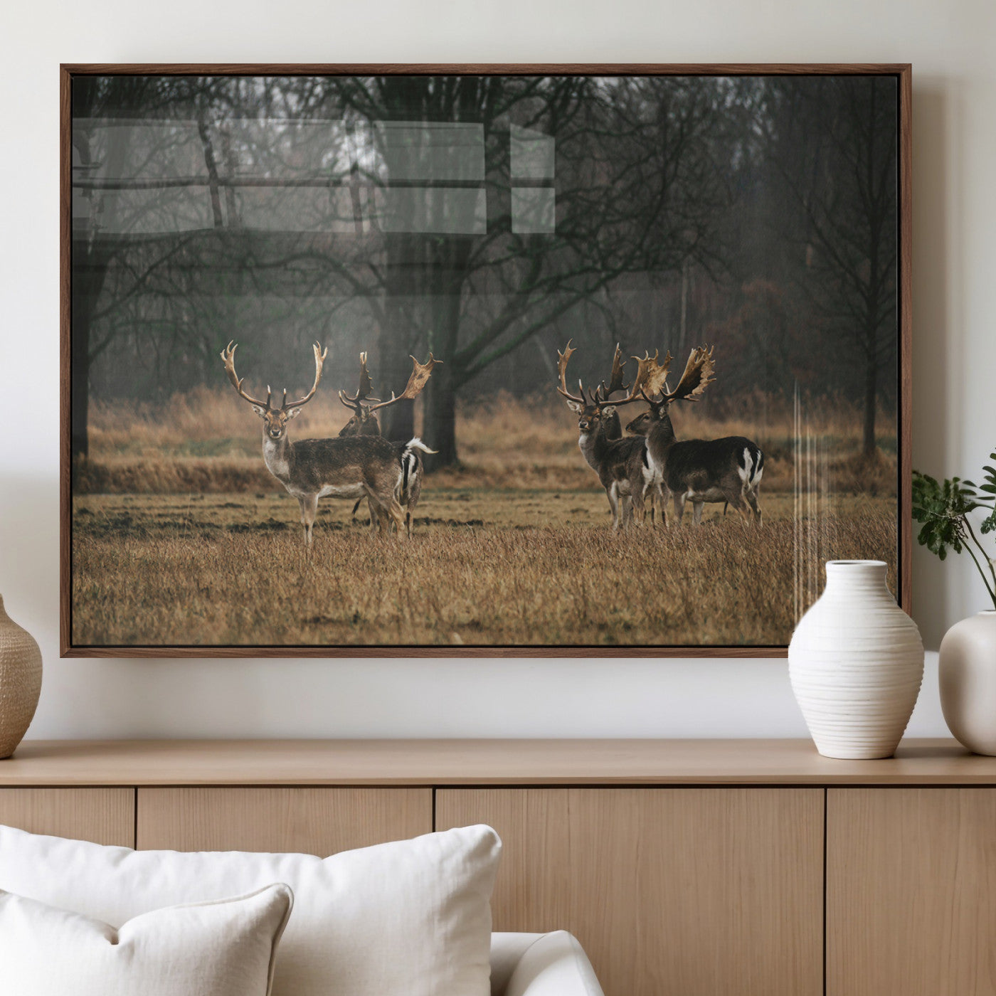 A group of majestic deer standing in a golden field with bare trees in the background, creating a peaceful woodland scene.