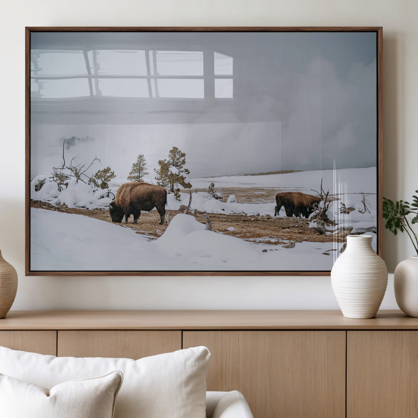 Two bison grazing in a snowy open landscape with misty hills in the background, creating a peaceful and rustic winter scene.