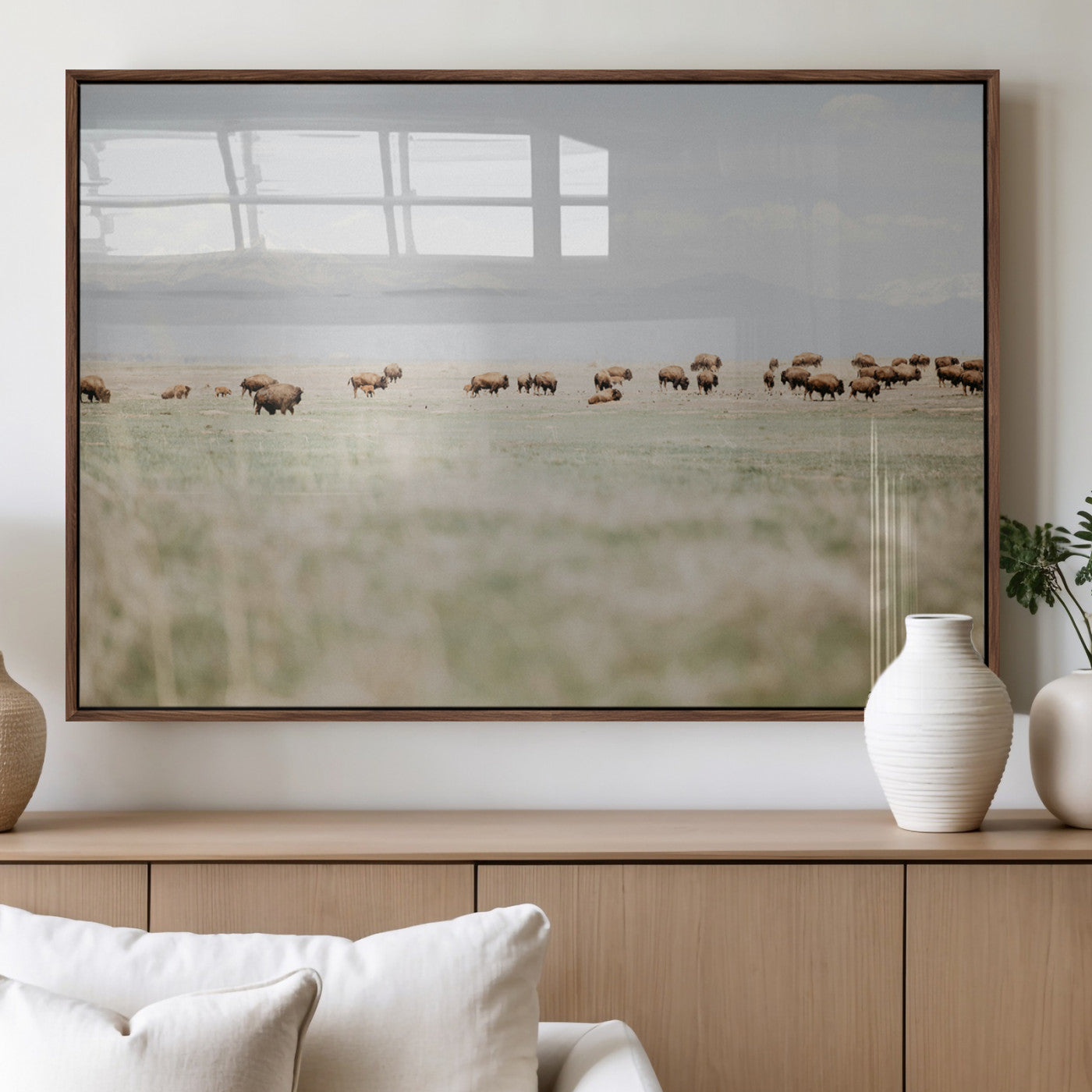 A herd of bison grazing in an open prairie with distant mountains under a soft sky, creating a serene and rustic Western landscape.
