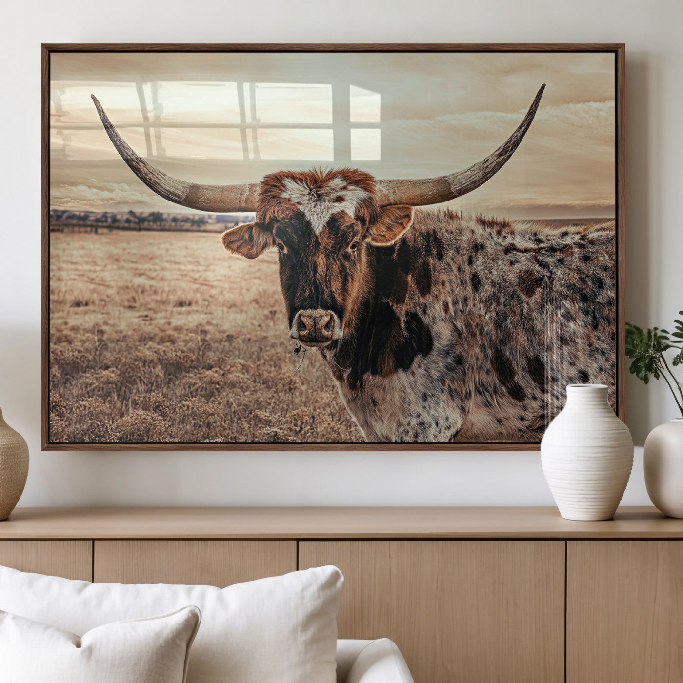 Close-up of a longhorn cow with distinctive curved horns standing in a dry grass field under a cloudy sky.