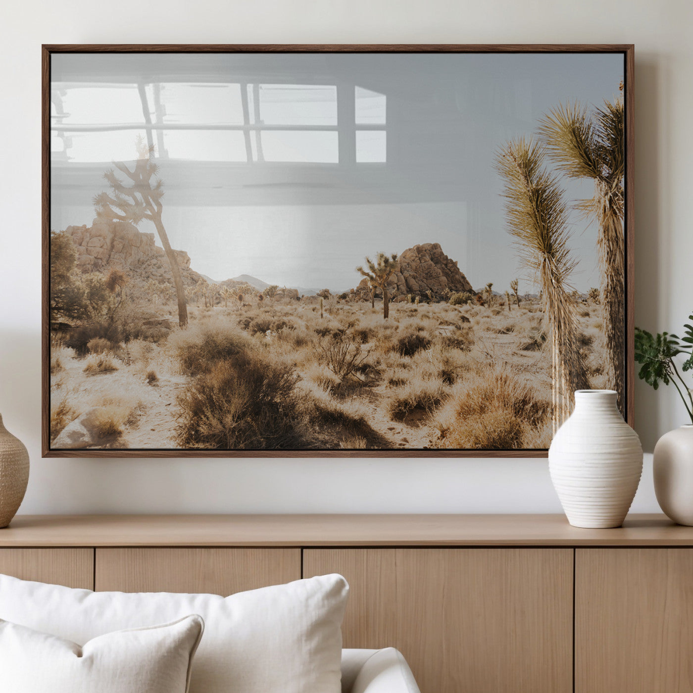 Sunlit desert landscape featuring Joshua trees, rocky formations, and dry bushes under a clear sky.