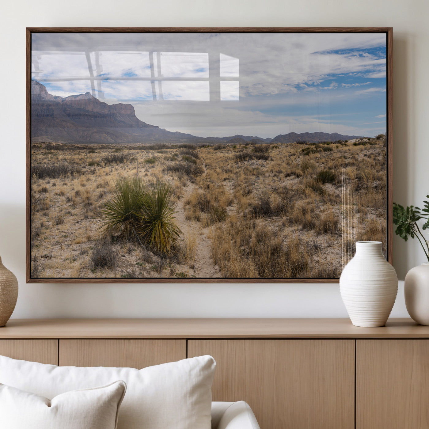 A scenic desert landscape with dry grasses, scattered shrubs, and a distant mountain range under a partly cloudy blue sky.