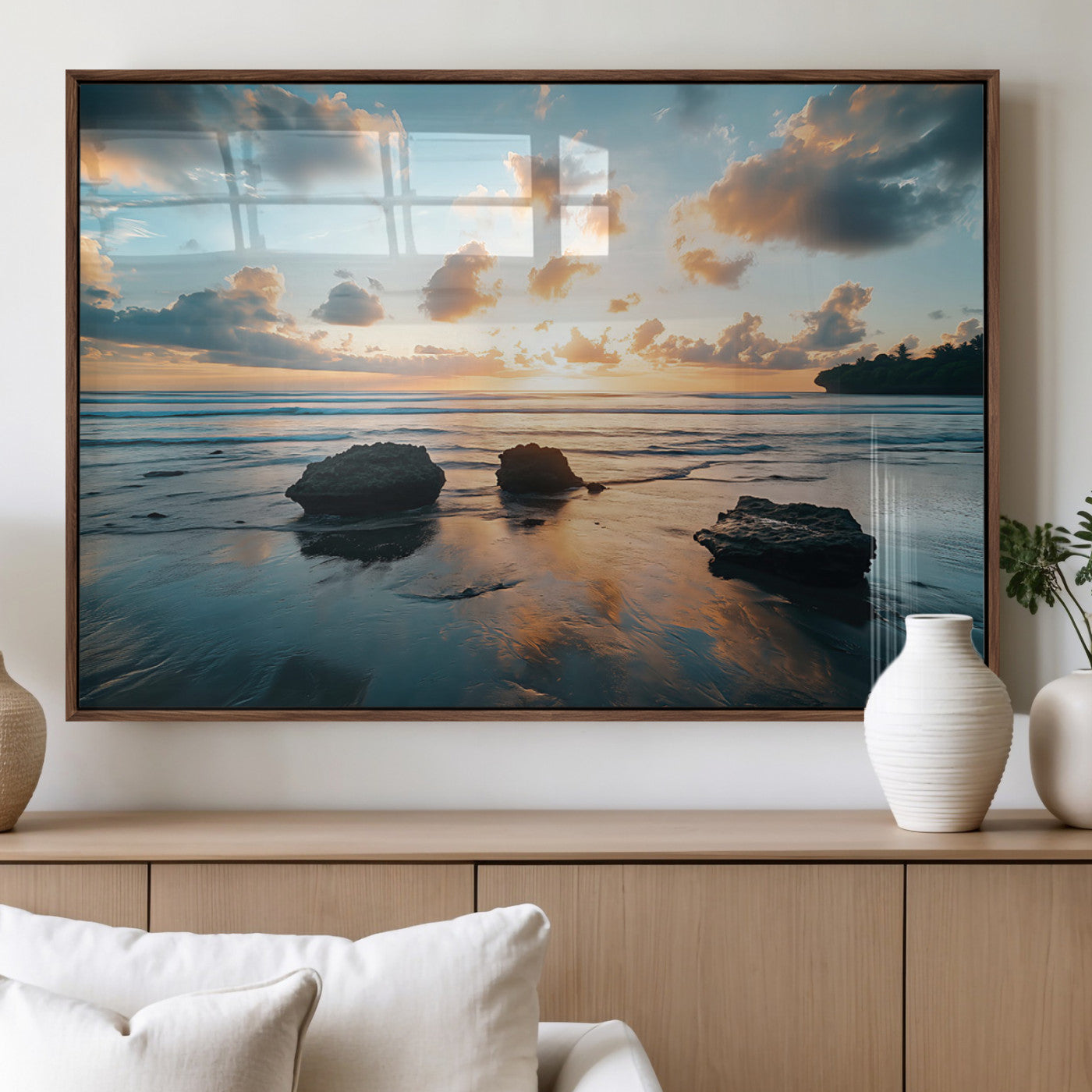 A serene beach at sunset with vibrant clouds, calm water, and rocks in the foreground reflecting the warm colors of the setting sun.
