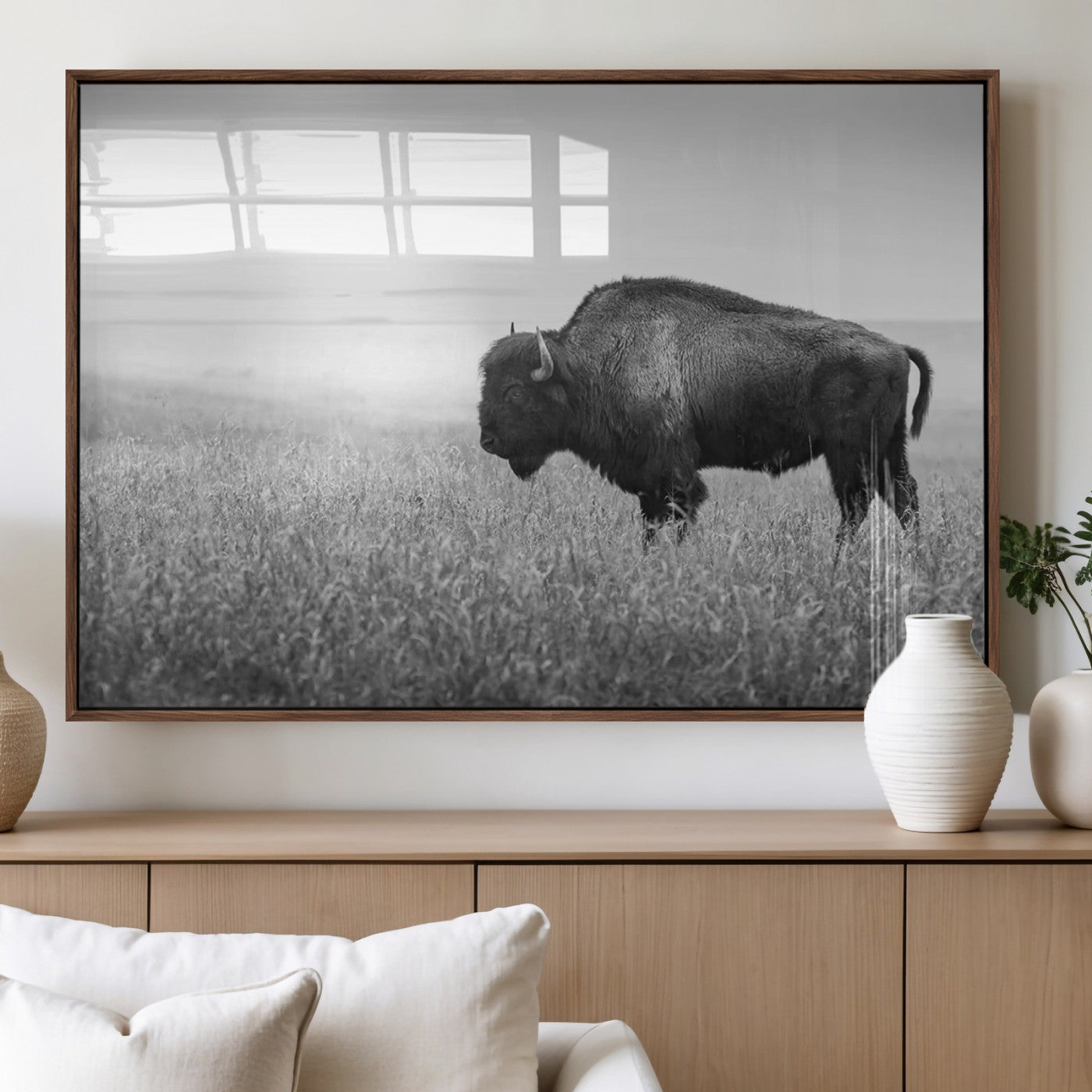 "Black and white image of a bison grazing in a vast field under an overcast sky."