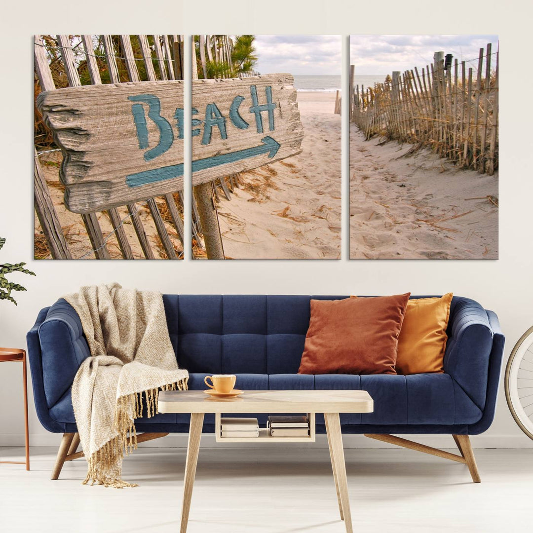 The Beach Is Calling You Wall Art Canvas Print features a sandy beach path with a wooden beach sign and arrow pointing to the ocean, beautifully displayed on museum-quality canvases.