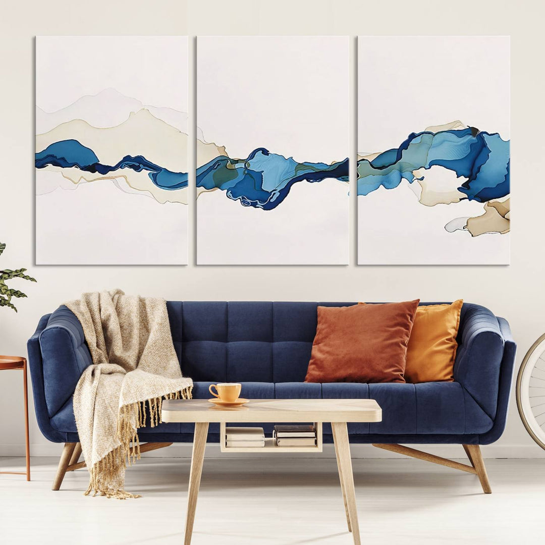 The modern living room showcases a set of three canvas prints with abstract blue art on museum-quality materials.