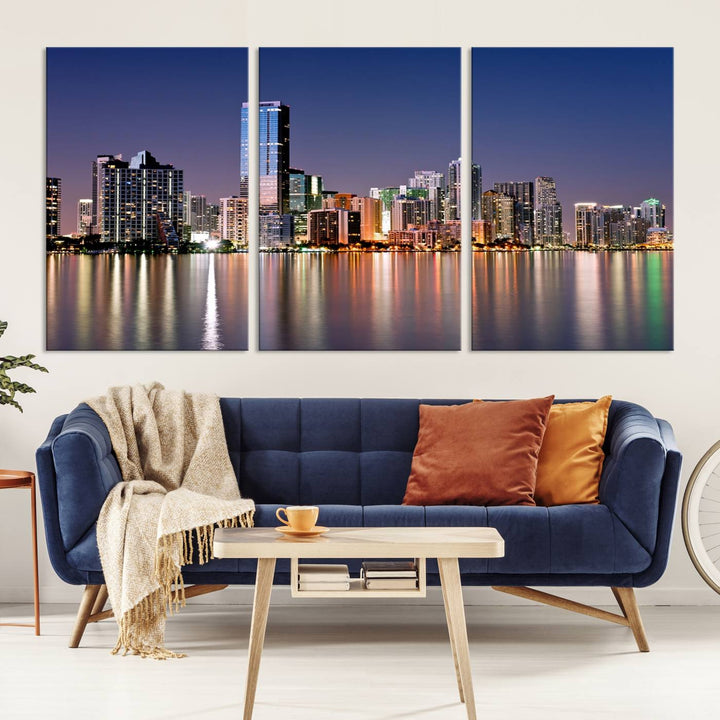 The Miami Skyline Canvas Wall Art Print showcases a vibrant night cityscape and beautifully captures the dazzling colorful lights reflecting on the water. This ready-to-hang triptych adorns the wall, creating a stunning visual centerpiece.