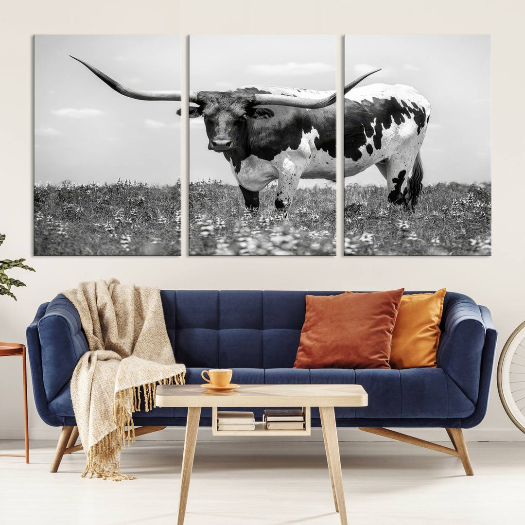 The Texas Black White Highland Longhorn Cow Wall Art Canvas Print, a gallery-quality triptych, elegantly adorns the wall, showcasing a striking black-and-white depiction of a longhorn cow in a field.