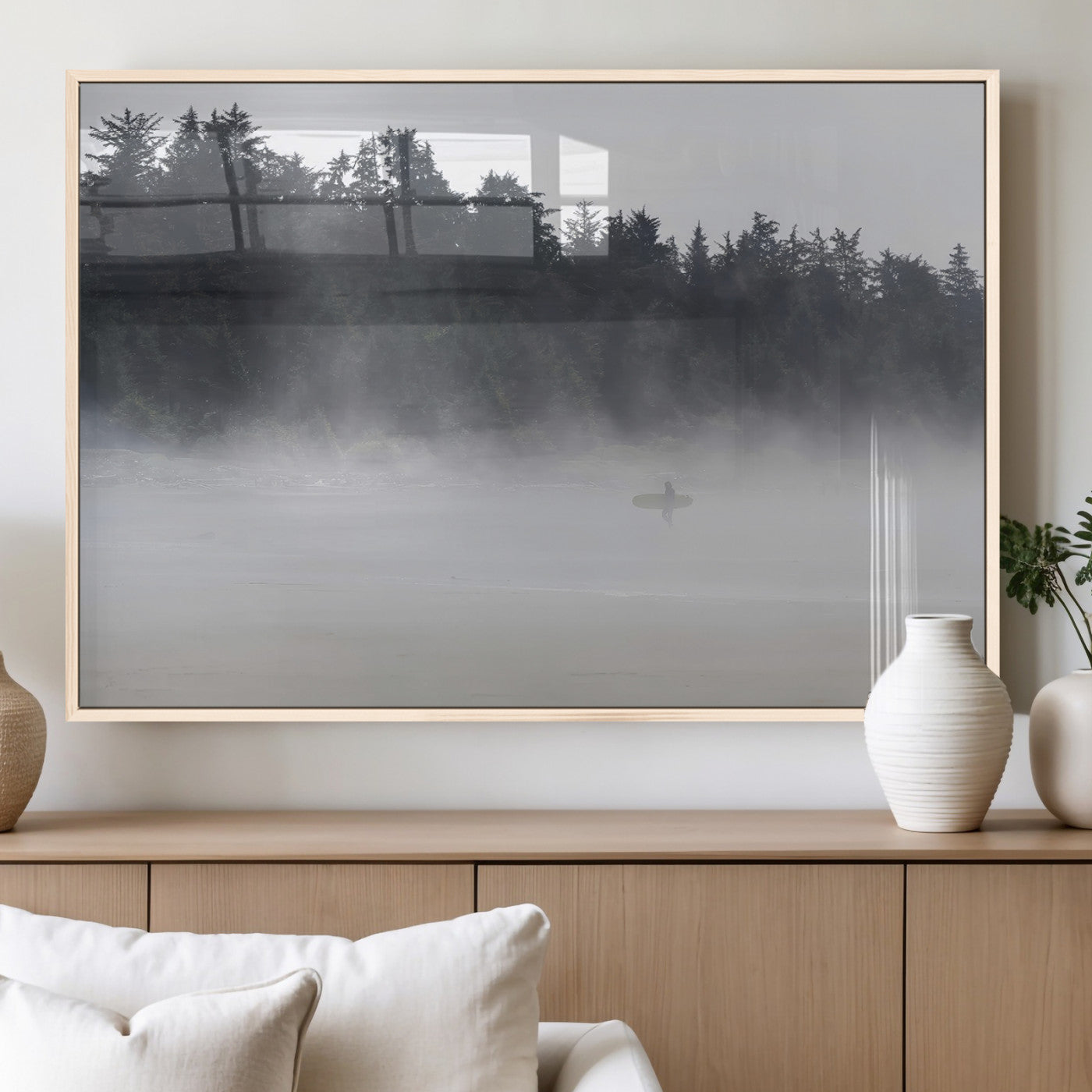 A lone surfer carrying a board through a misty shoreline, surrounded by dense trees and fog, creating a peaceful and mysterious coastal scene.
