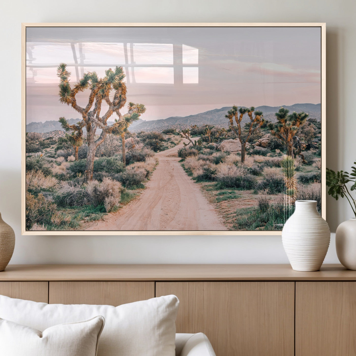 A dusty road winding through Joshua Tree National Park, framed by iconic twisted trees and warm desert tones under a soft pastel sky.