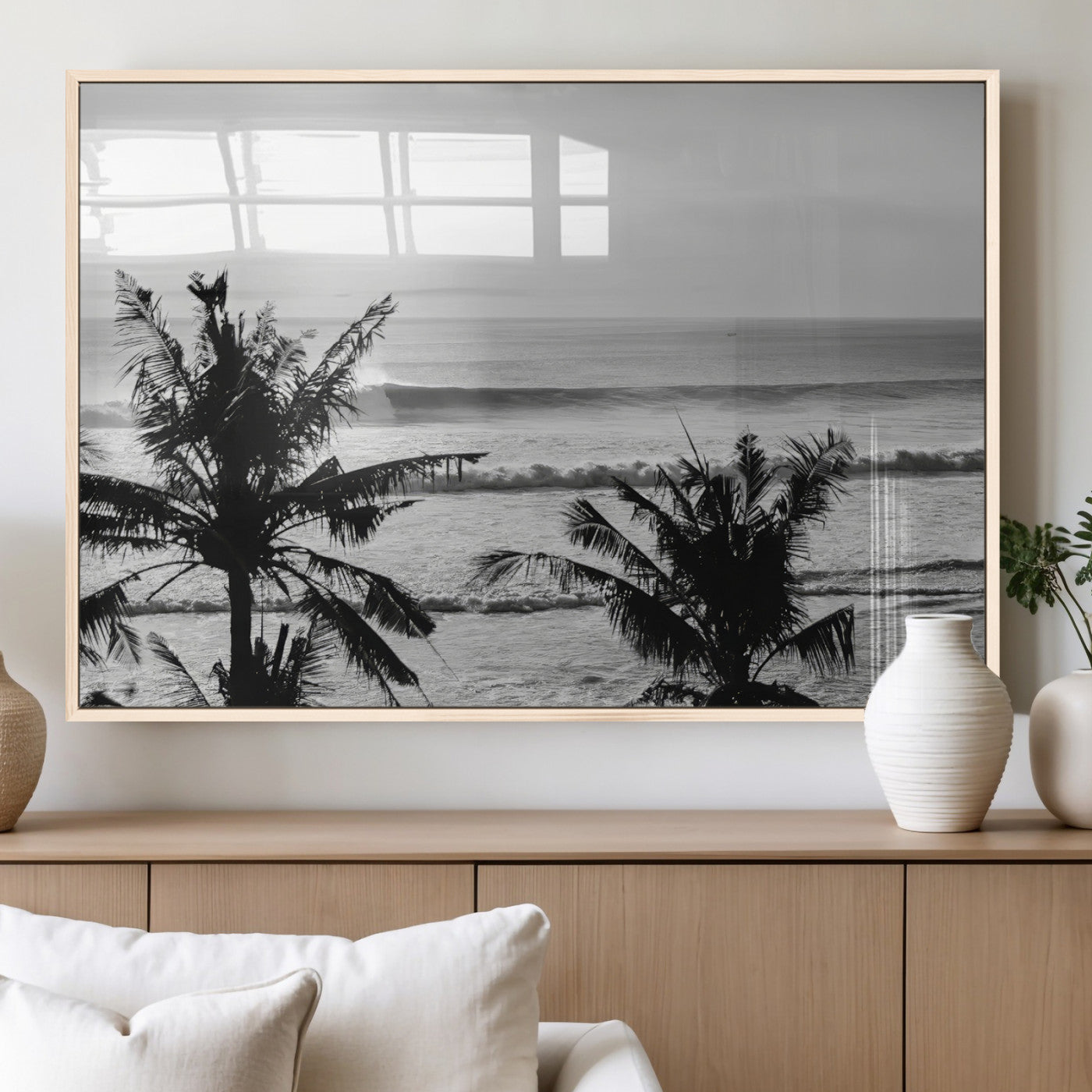 Black and white view of ocean waves crashing on a tropical coastline, framed by silhouetted palm trees under a vast, open sky.