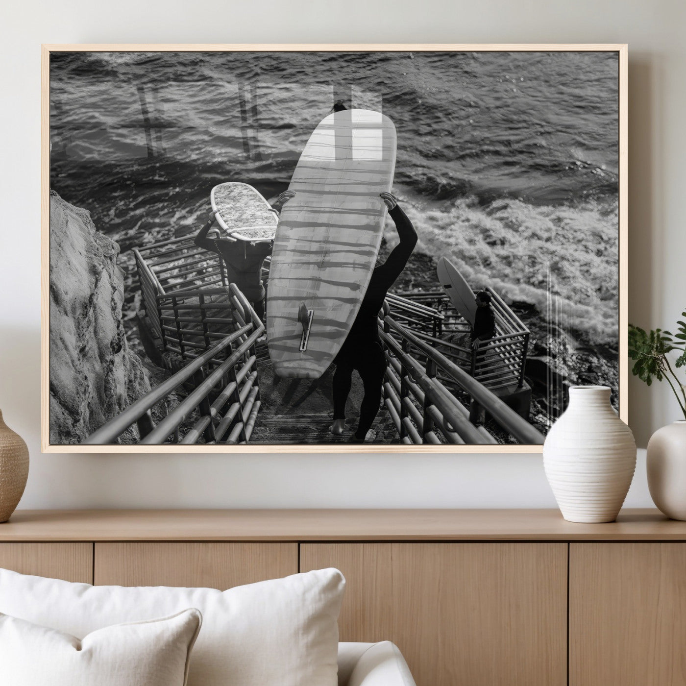 Black and white photo of surfers carrying boards down a rugged cliffside stairway, capturing a bold and adventurous coastal scene.