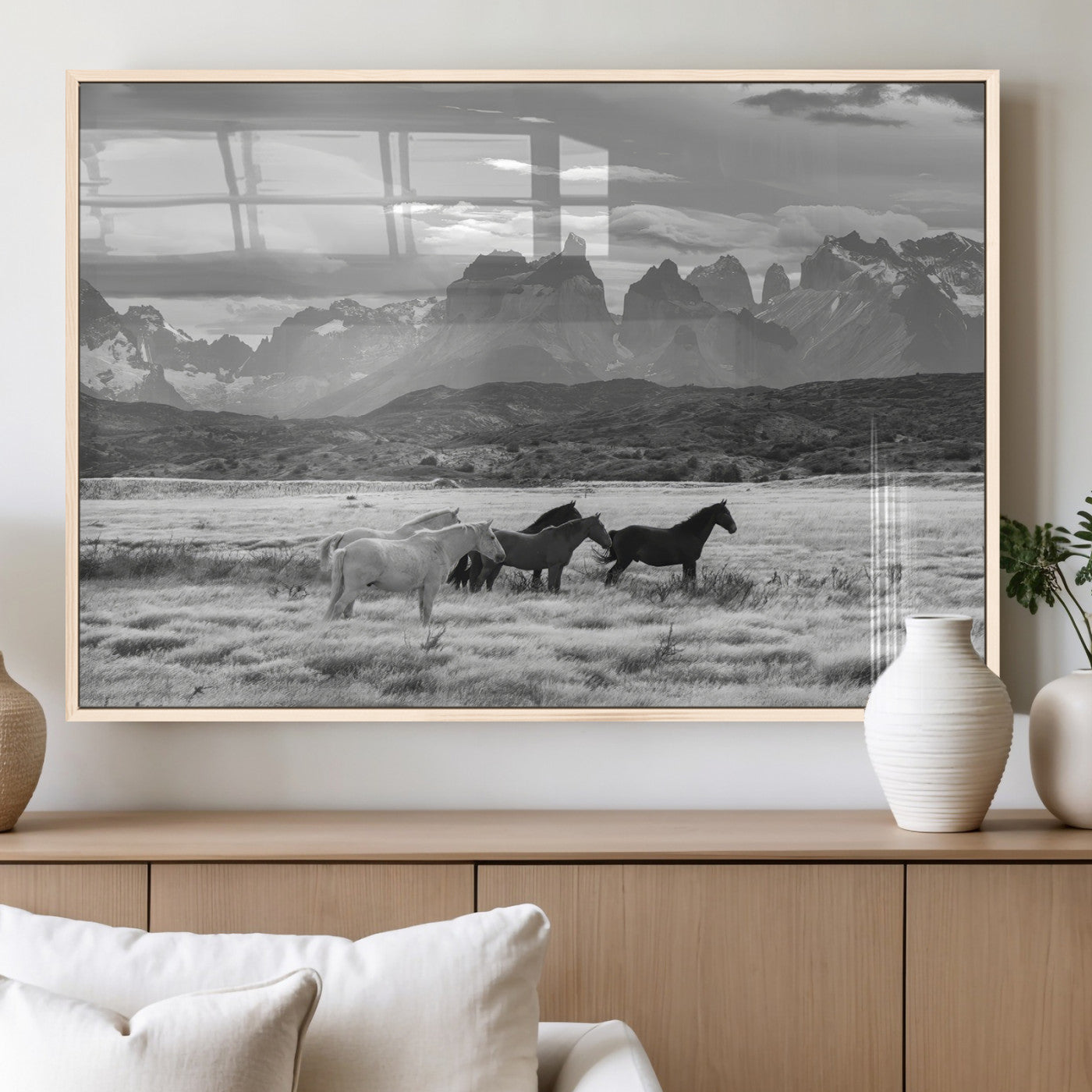 A black and white landscape of wild horses grazing in a vast grassland with towering mountains in the background, creating a moody and rustic western aesthetic.