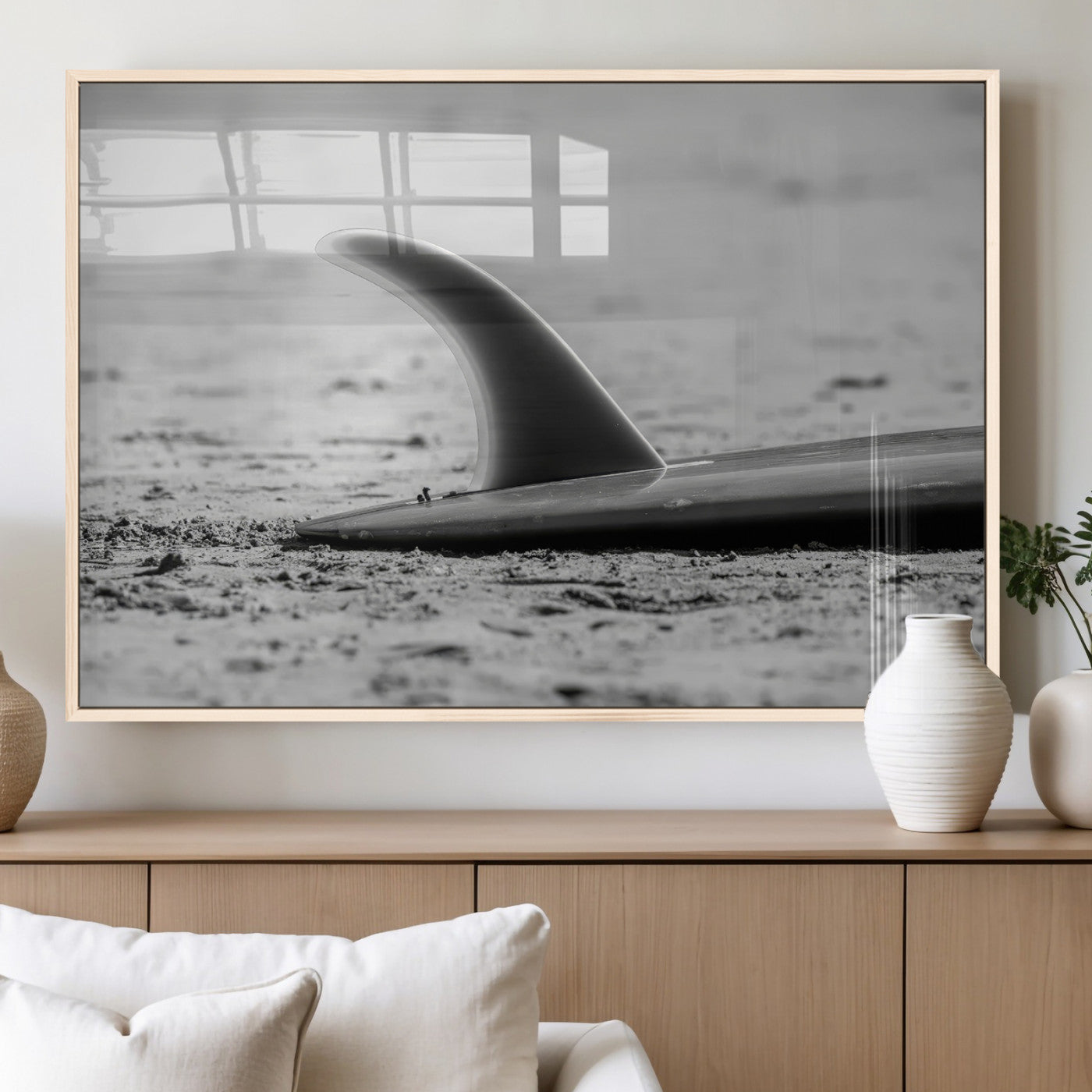A black and white close-up of a surfboard fin resting on the sandy shore, highlighting minimalist beach aesthetics and classic surf culture.