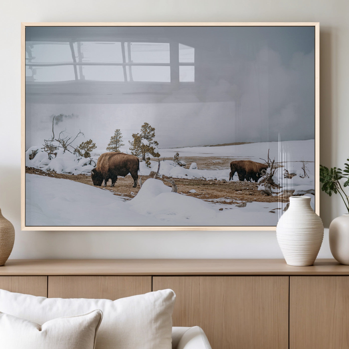 Two bison grazing in a snowy open landscape with misty hills in the background, creating a peaceful and rustic winter scene.