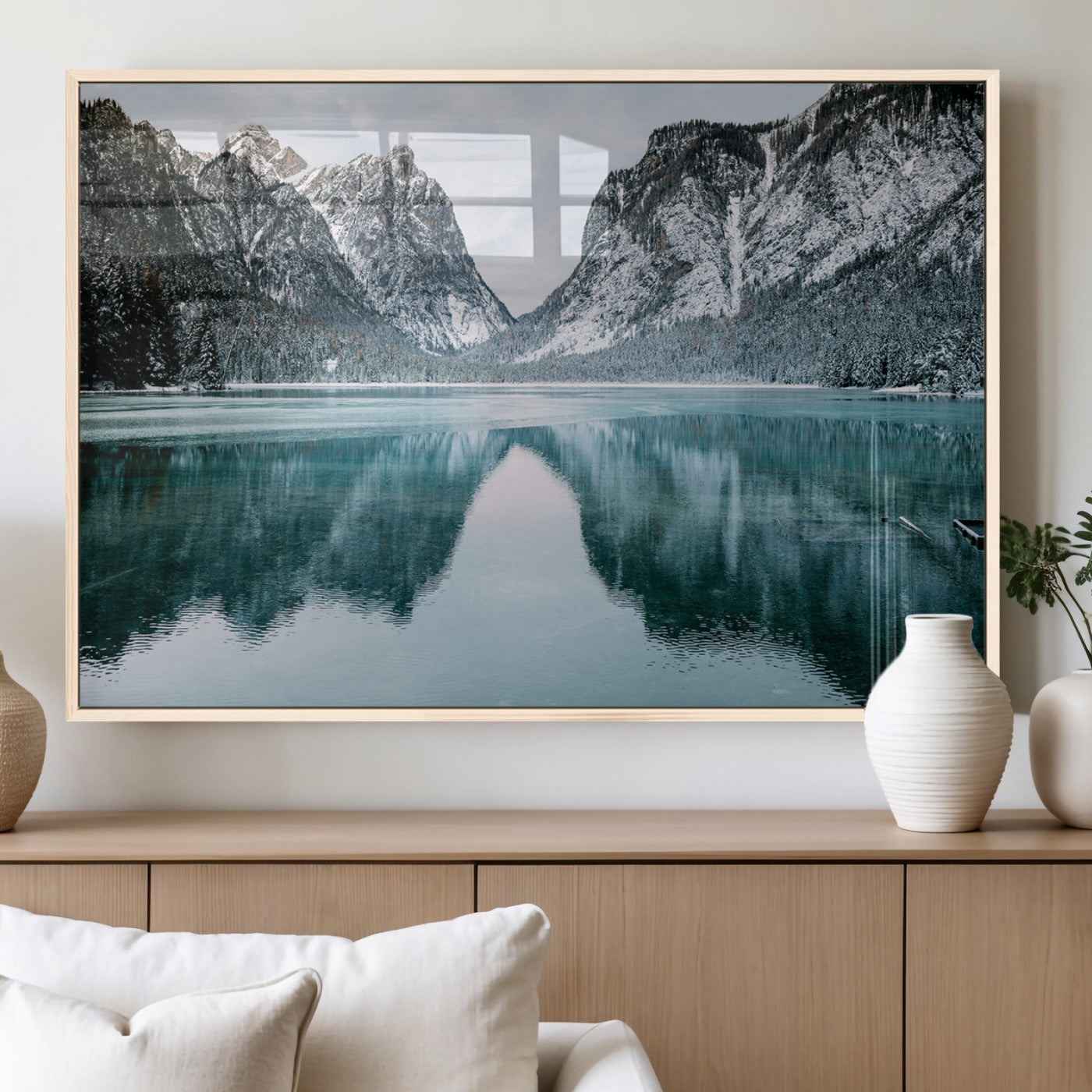 Crystal-clear alpine lake reflecting snow-covered mountains, surrounded by evergreen trees, creating a serene and tranquil winter landscape.