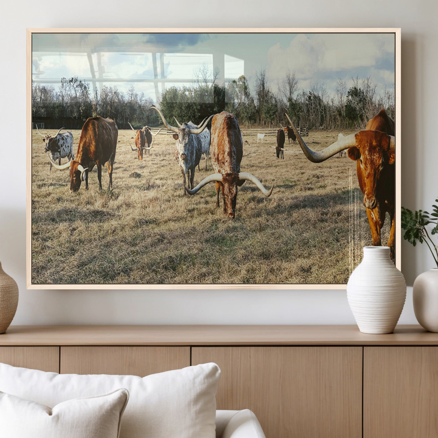 A herd of Texas Longhorn cattle grazing in an open field under a partly cloudy sky, capturing a rustic and Western ranch aesthetic.